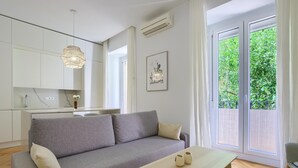 Een moderne woonkamer met een grijze bank, een houten salontafel en uitzicht op groen door grote ramen.