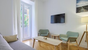 Een moderne woonkamer met een bank, twee fauteuils, een salontafel, een aan de muur bevestigde televisie en een lamp.