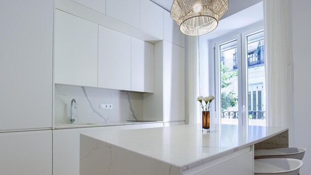 Een moderne keuken met witte kasten, een marmeren aanrecht en een houten stoel.