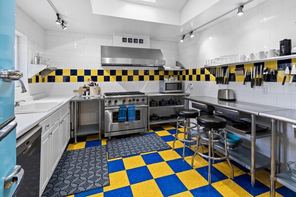 Una cocina moderna con baldosas blancas, piso a cuadros, electrodomésticos de acero inoxidable y taburetes de bar.