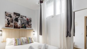Ein Hotelzimmer mit einem großen Bett, weißer Bettwäsche, einem hölzernen Kopfteil und drei schwarz-weißen Kunstwerken an der Wand.