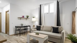 Ein modernes Wohnzimmer mit einer Couch, einem Couchtisch, einem Esstisch mit Stühlen und einem kleinen Beistelltisch mit Pflanze.