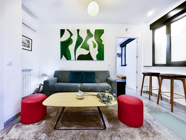 A modern living room with a grey sofa, red ottomans, a wooden coffee table, and a green abstract painting on the wall. - Charming Madrid Principe Pio (Madrid)