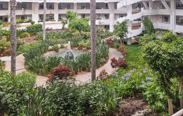 Hotel de varios niveles con un patio central que cuenta con una fuente de agua, rodeado de vegetación exuberante y diversas plantas.