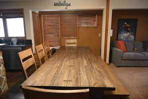 Un coin repas avec une table et des chaises en bois, un coin cuisine équipé d’un lave-vaisselle, et un salon avec un canapé et un tableau.