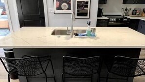 Une cuisine moderne dotée d’un grand îlot central, de chaises noires et de luminaires suspendus.