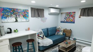 A compact living space with a kitchenette, a sofa, a coffee table, and two bar stools. - Cozy NYC on the Island (West Hempstead)