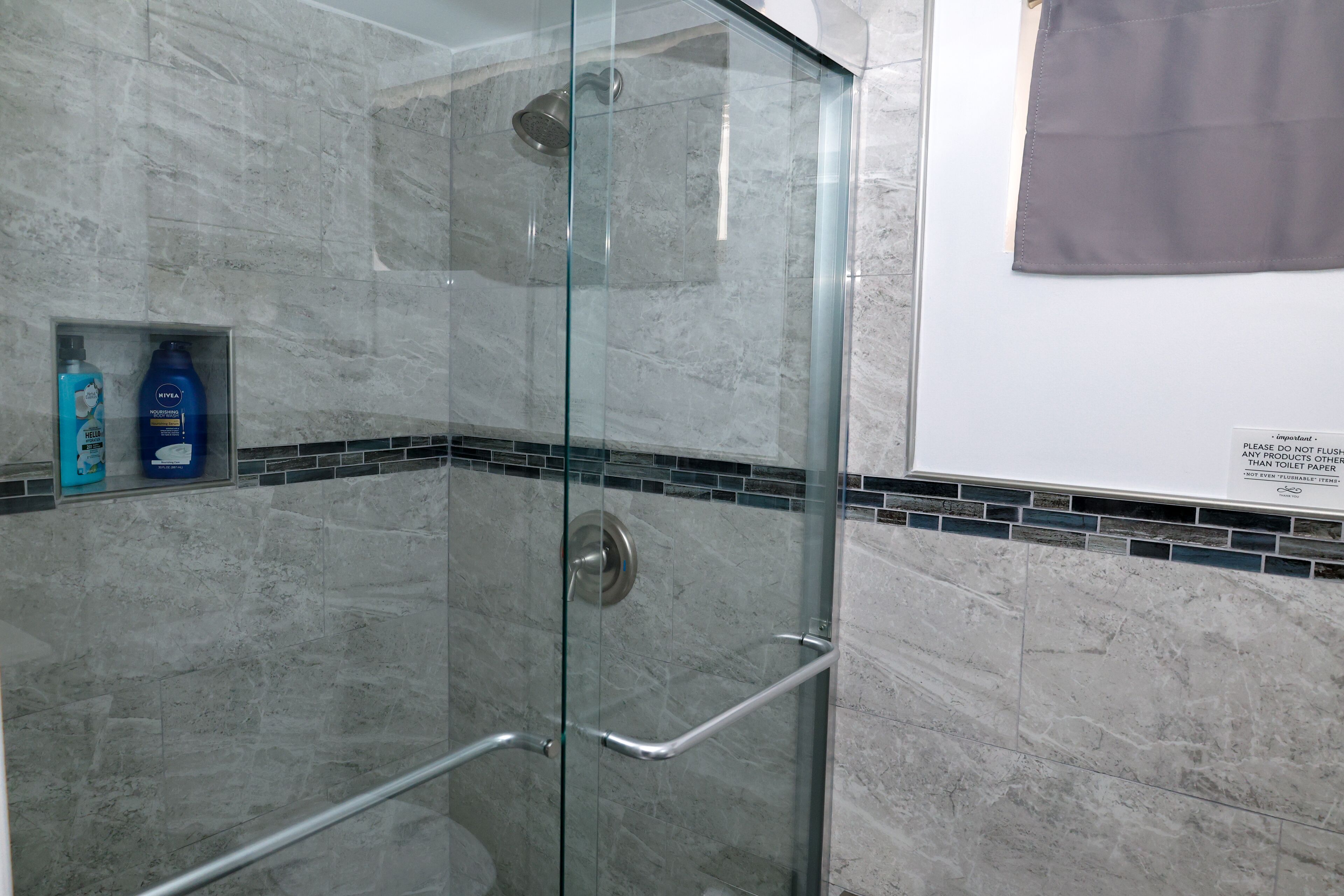 Een douche met glazen wand, een marmeren muur, een handdoekhouder en toiletartikelen aan de wand.