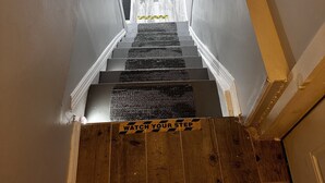 A staircase with caution tape and signs warning to watch your head and step. - Cozy NYC on the Island (West Hempstead)