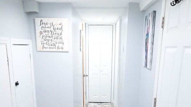 A hallway with a patterned rug, white doors, and a wall with inspirational quotes. - Cozy NYC on the Island (West Hempstead)