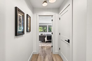 A hallway with a door leading to a room with a bed and a window.