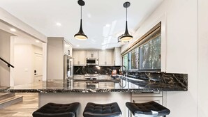 Una cocina moderna con encimera de mármol negro, electrodomésticos de acero inoxidable y tres taburetes negros.