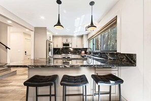 A modern kitchen with a black marble countertop, stainless steel appliances, and three black bar stools. - The Seasons Tahoe 4bdr Cabin (Tahoe Vista)