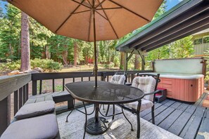A deck with a table and chairs, an umbrella, and a hot tub. - The Seasons Tahoe 4bdr Cabin (Tahoe Vista)