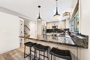 Una cocina moderna con encimera de mármol, electrodomésticos de acero inoxidable y taburetes de bar negros.