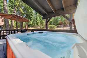 A hot tub under a wooden pergola with a view of a forest.