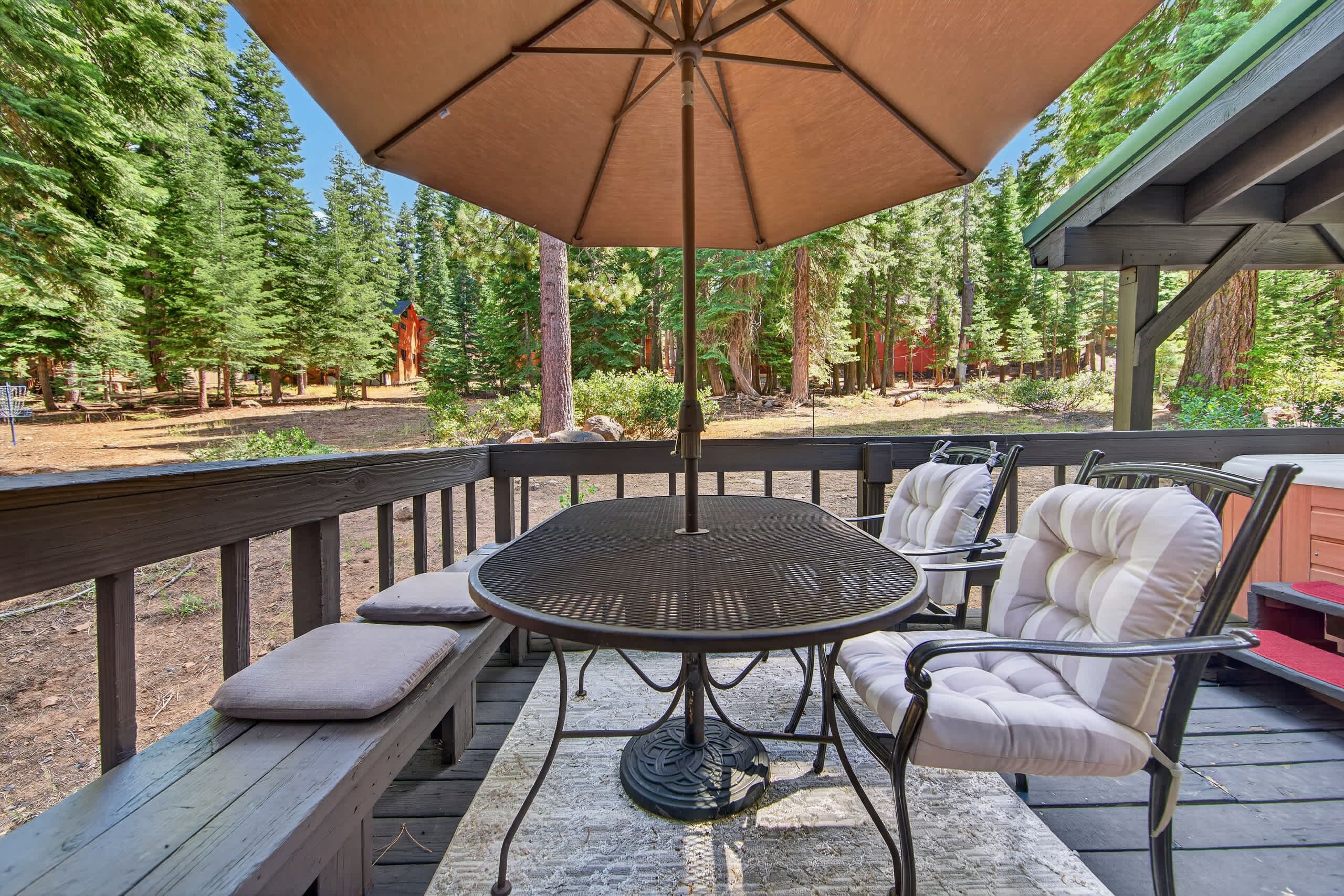 A wooden deck with a round table and chairs, an umbrella, and a view of a forested area.