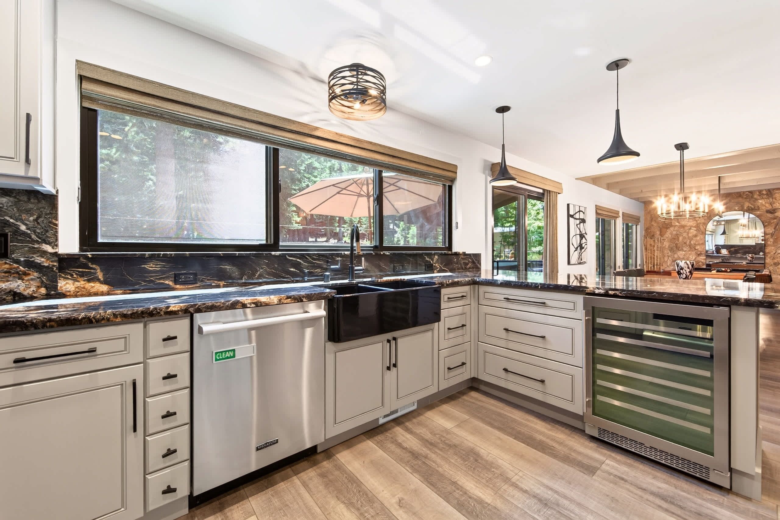 A modern kitchen with a dishwasher, double sink, and a large window with an umbrella.