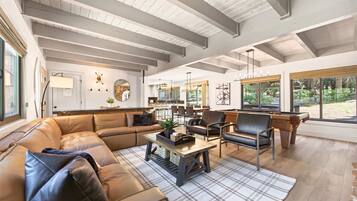 A spacious living area with a high ceiling, a large sofa, a coffee table, and a view of the outdoors through large windows.