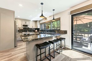 A modern kitchen with a large island, bar stools, and a view of the outdoors through a large window.