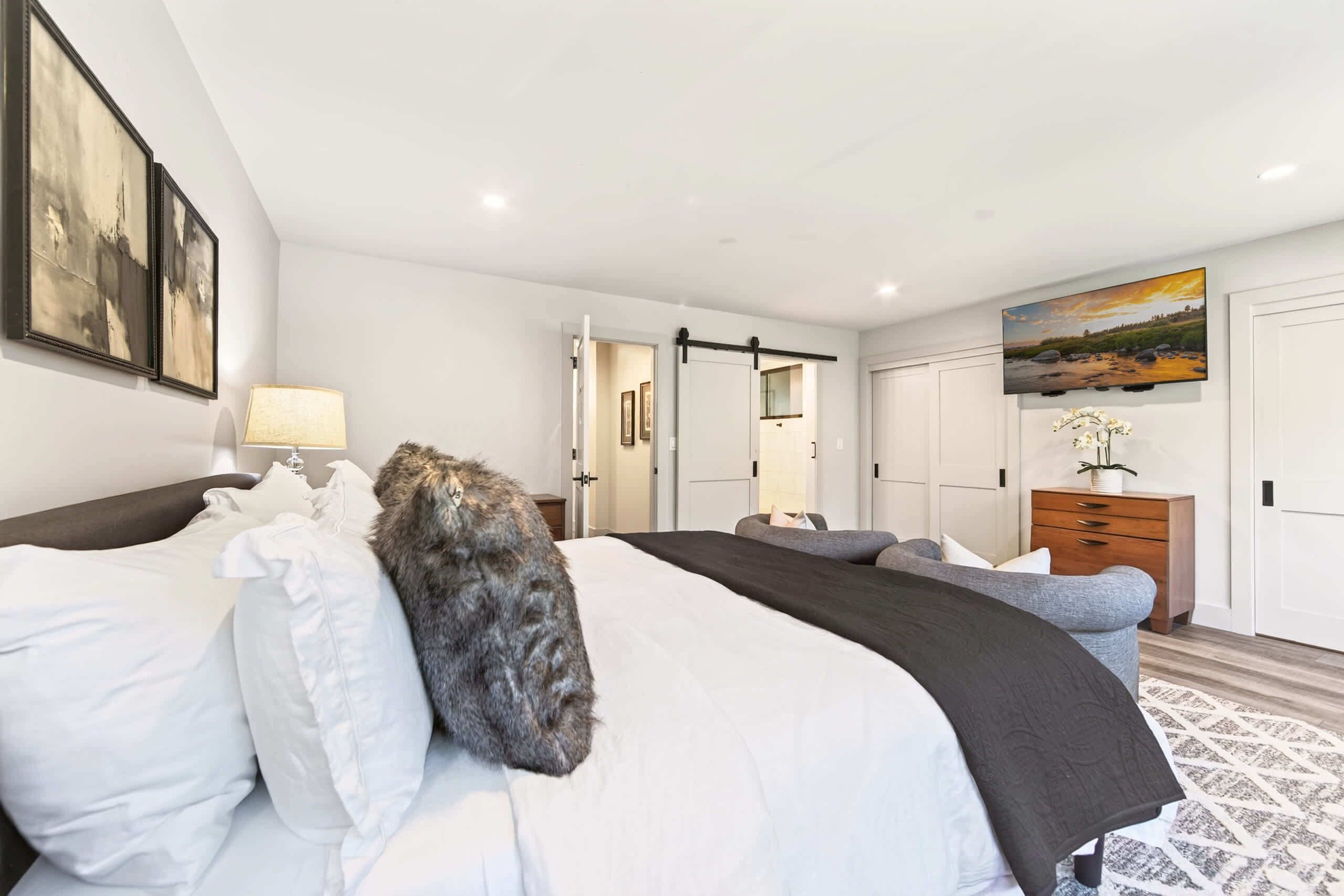 A modern bedroom with a large bed, a bedside table, a dresser, and a television on the wall.