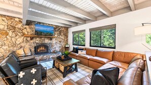 Una sala de estar acogedora con chimenea de piedra, sofá de cuero y televisión montada arriba.
