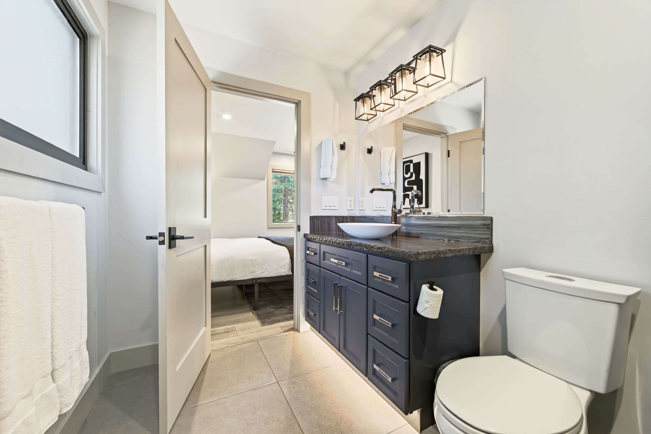 A modern bathroom with a large mirror, a white toilet, dark cabinets, and a sink with a bowl.