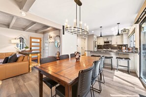 A modern kitchen with stainless steel appliances, a wooden dining table, and bar stools.