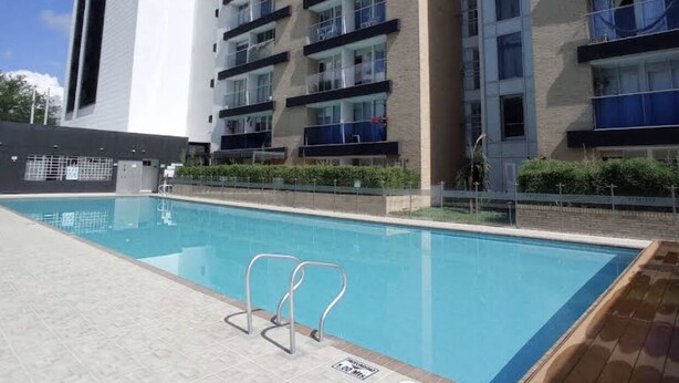 A modern building with a swimming pool, featuring a clear sky and a tiled deck.