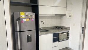 A compact kitchen with a stainless steel refrigerator, a built-in oven, and a sink.