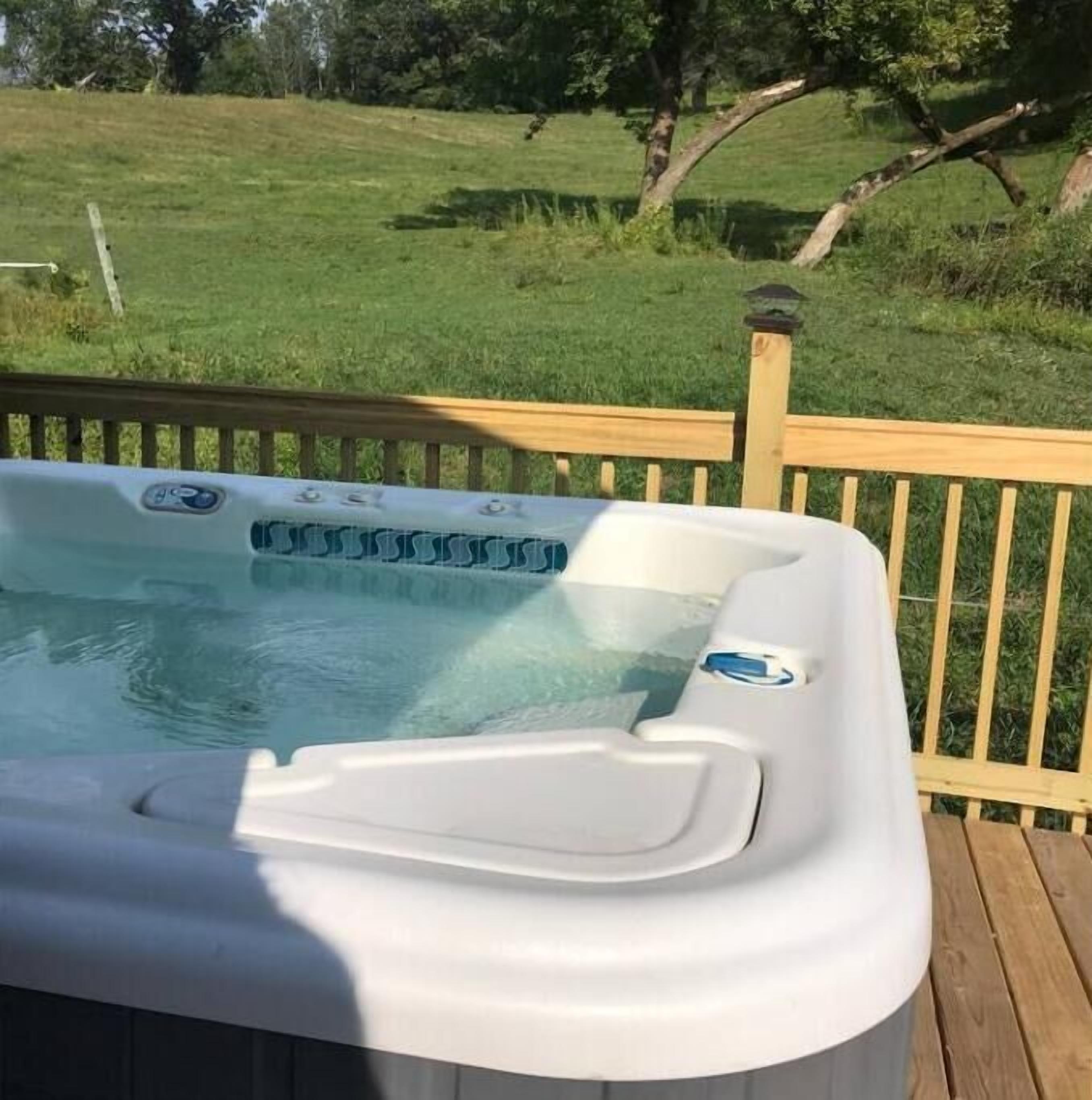 Un bain à remous sur une terrasse en bois, avec un paysage verdoyant en arrière-plan.