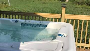 Un bain à remous sur une terrasse en bois, avec un paysage verdoyant en arrière-plan.