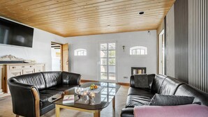 A living room with two black leather sofas, a glass coffee table, and a wooden ceiling.