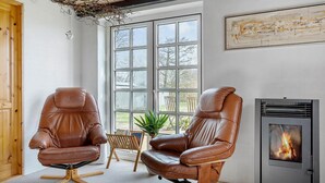 A room with two leather chairs, a wooden floor, a fireplace, and a large window with a view of the outdoors.