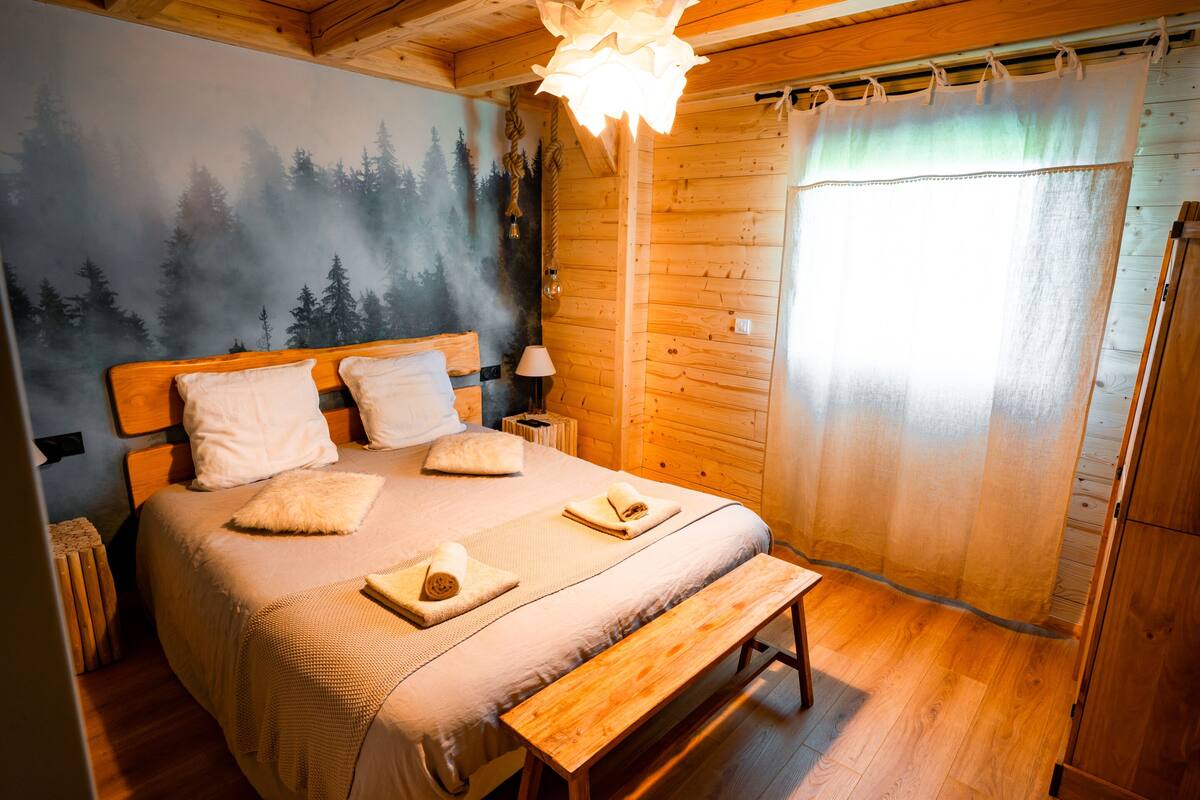 Ein gemütliches Schlafzimmer in einer Holzhütte mit Bett, Kissen, einer Bank, einem Nachttisch und einer Wandmalerei.