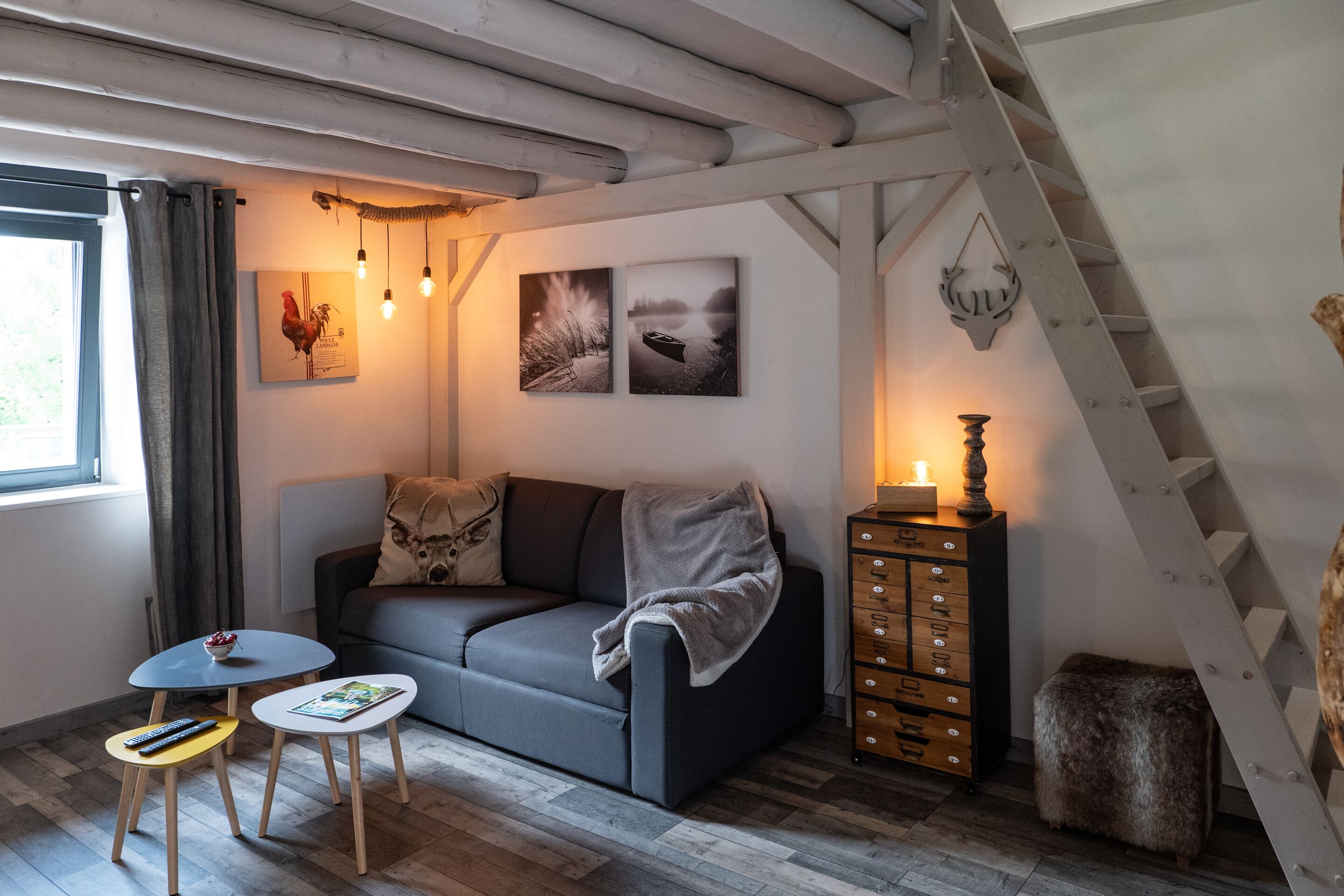 A cozy living room with a sofa, two small tables, a cabinet, and a staircase.