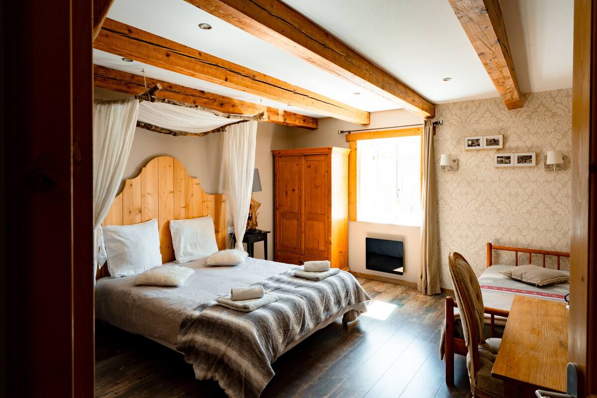 Ein Schlafzimmer mit einem großen Bett, Holzbalken, einem Holzschrank und einem kleinen Tisch mit Stuhl.