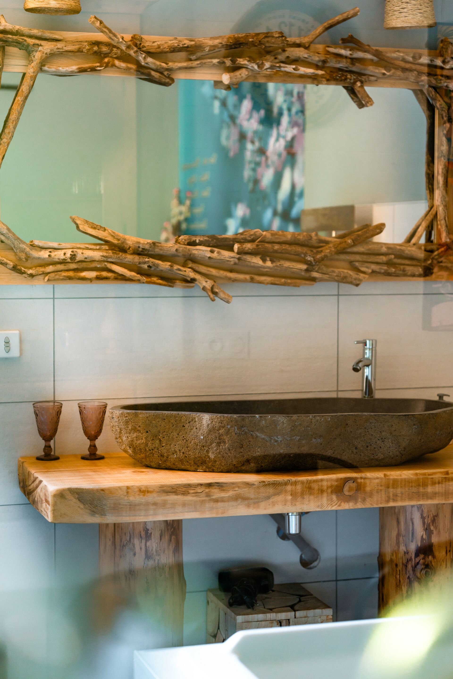 Un baño con un espejo de madera rústica, un lavabo de piedra y una bañera blanca.