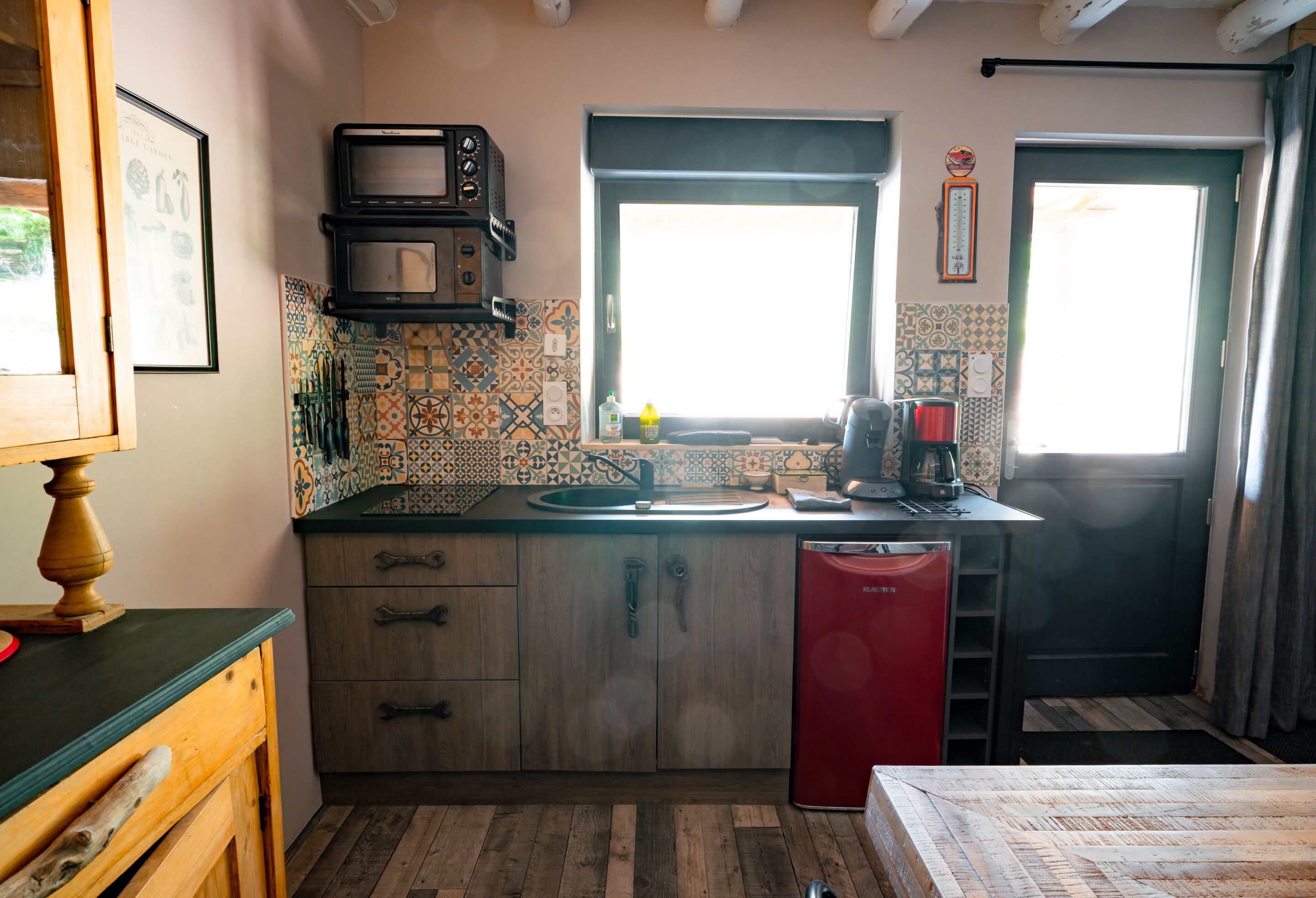 Une cuisine compacte avec un plan de travail en bois, un lave-vaisselle rouge et une fenêtre donnant sur un paysage agréable.