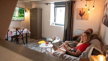 Un salon confortable avec un canapé, une table à manger et des chaises, une fenêtre avec des rideaux et un luminaire fixé au mur.