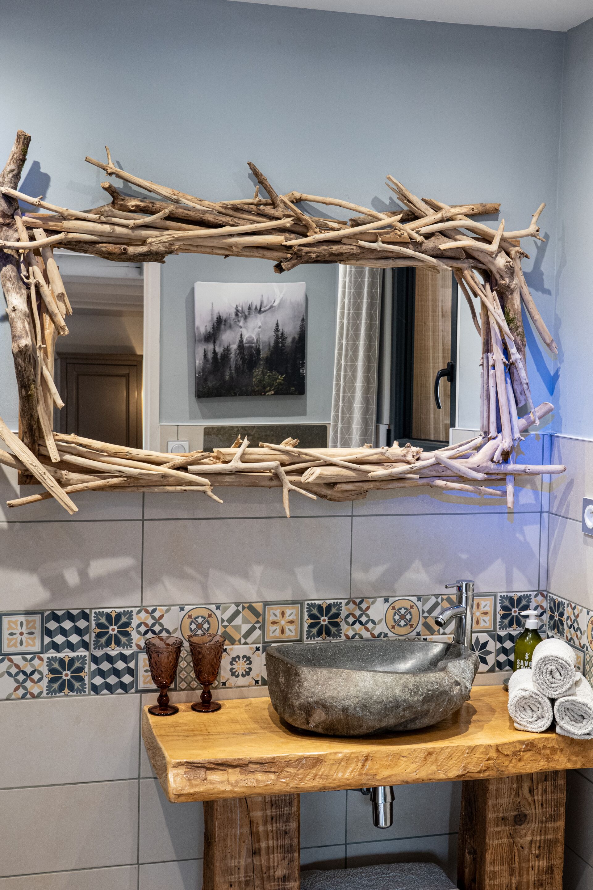 Un baño de estilo rústico, con un espejo de marco de madera natural, un lavabo de piedra y una salpicadura de azulejos con diseños geométricos.