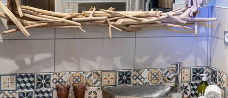 Un baño de estilo rústico, con un espejo de marco de madera natural, un lavabo de piedra y una salpicadura de azulejos con diseños geométricos.