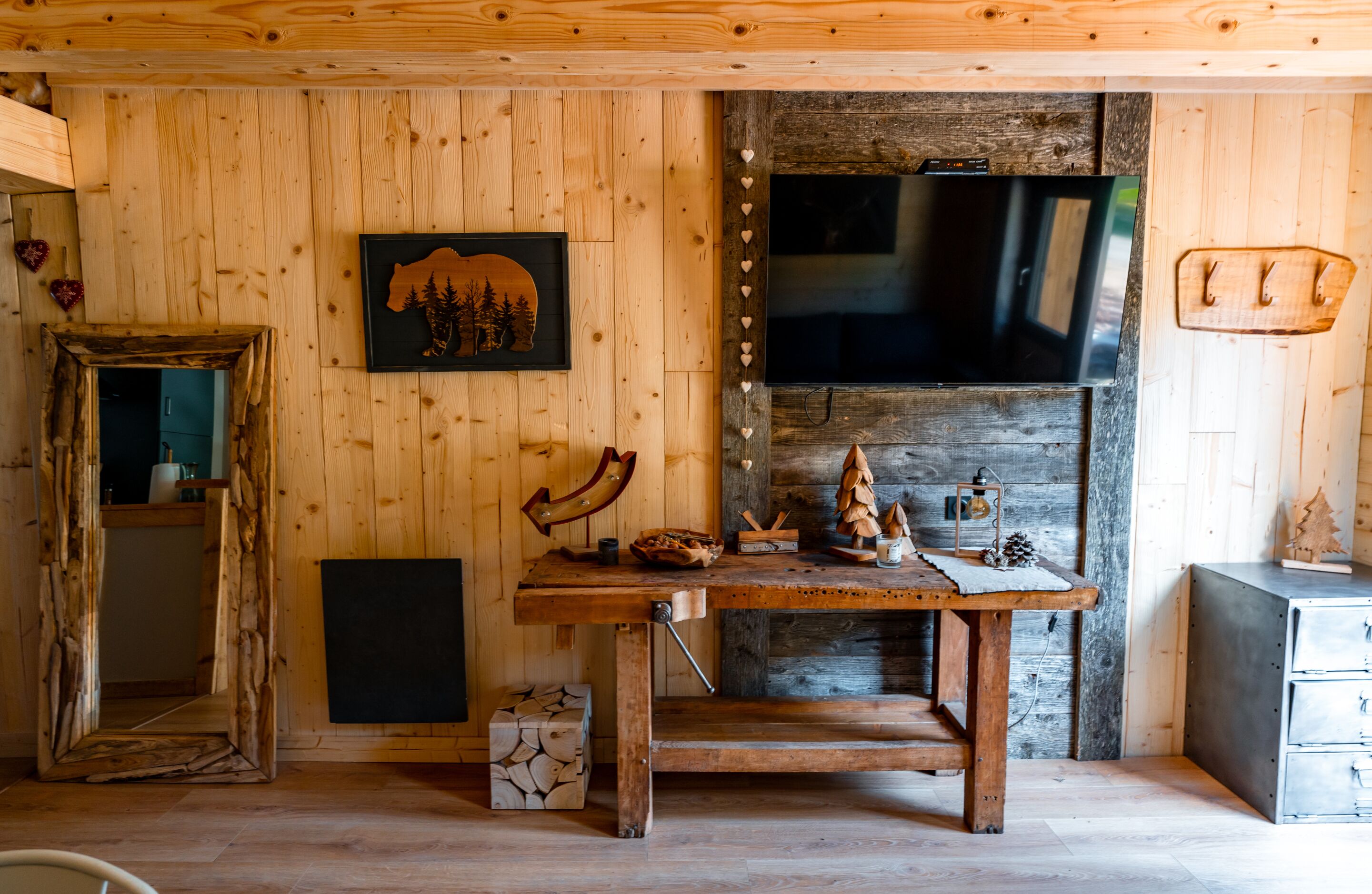 A rustic wooden interior with a wooden table, a framed picture of a bear, a fireplace, and a television.