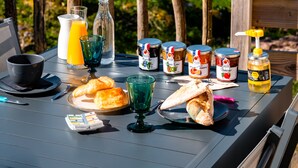 Une table de petit-déjeuner avec des croissants, une bouteille de jus d’orange et des pots de confiture.