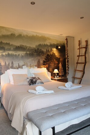 Ein Schlafzimmer mit einem Bett, Kissen, einem Nachttisch mit Lampe, einer Leiter und einem Wandgemälde von einem Wald.