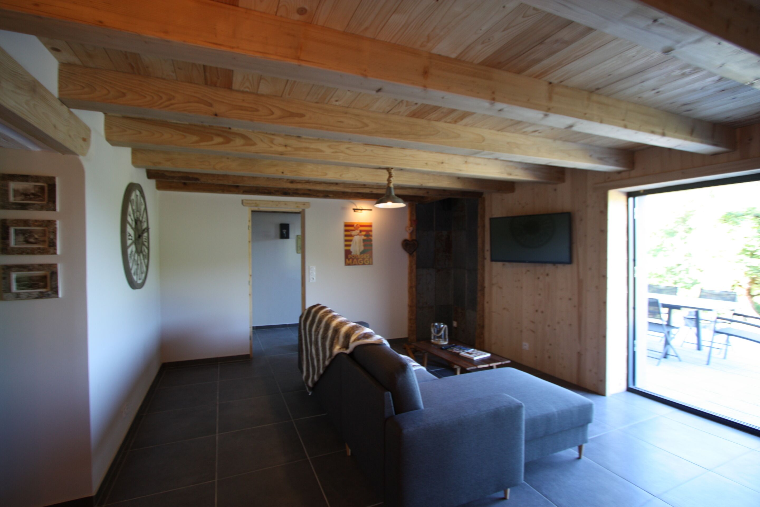 A modern living room with a sofa, a coffee table, and a fireplace. There is a large window providing natural light and a view of the outdoors.