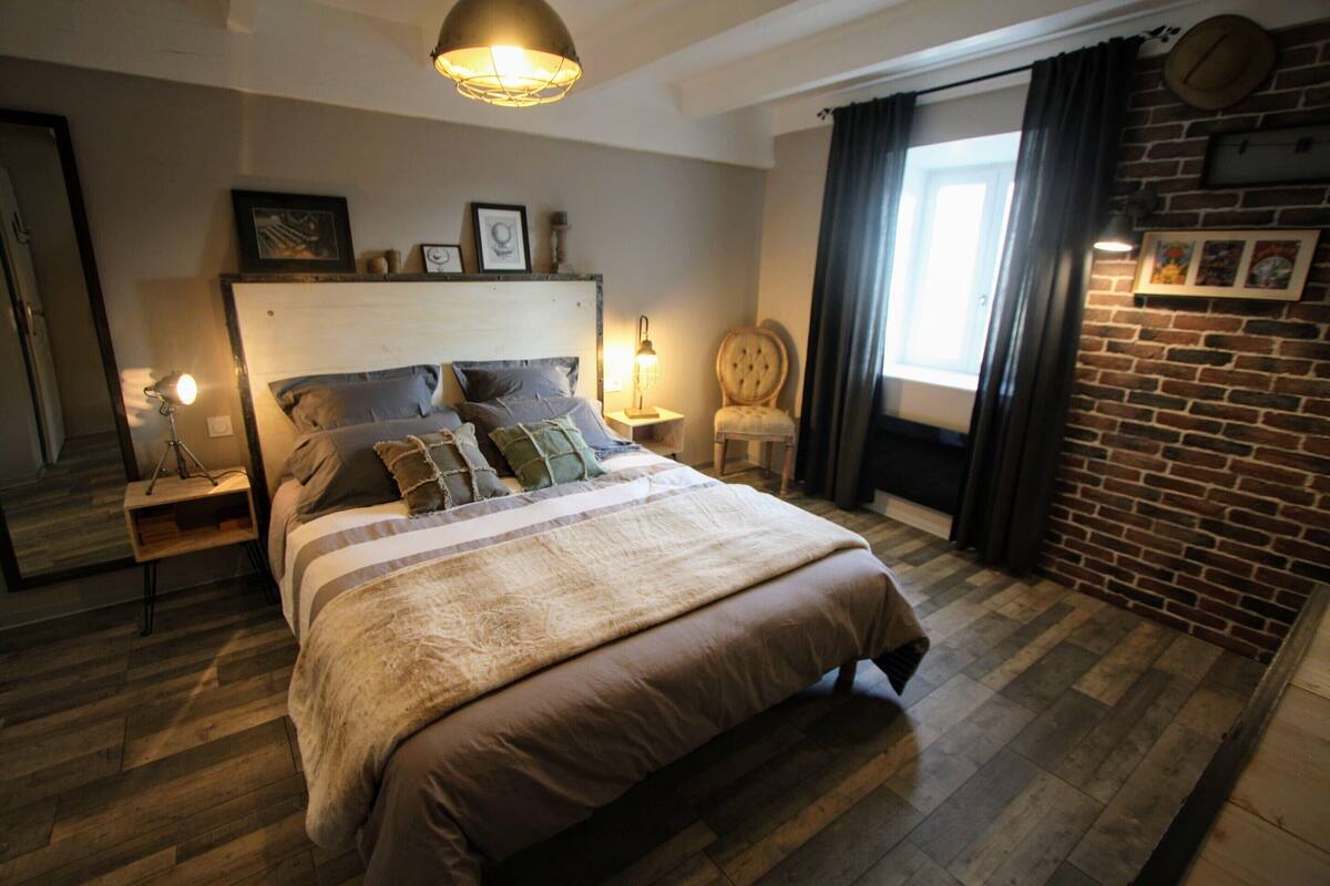 Ein Schlafzimmer mit einem großen Bett, Holzboden, einer Ziegelwand und einem Vorhangfenster.
