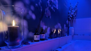 Une salle de bain avec une bougie allumée, deux flacons de lotion et des objets décoratifs sur une étagère.