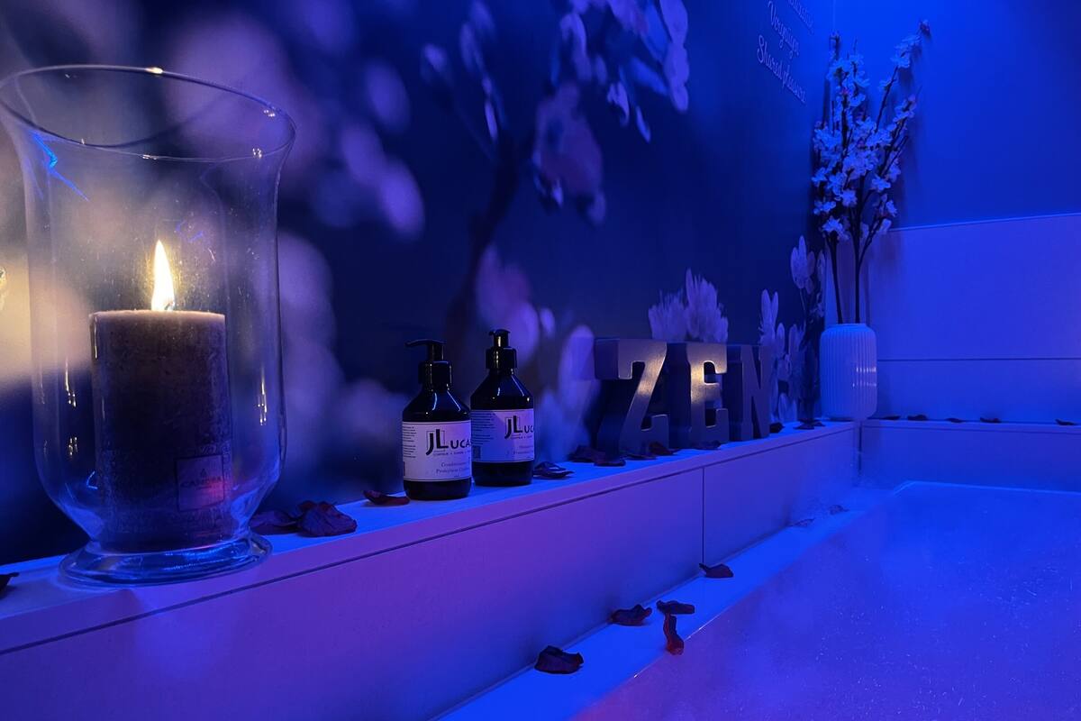 Ein Badezimmer mit brennender Kerze, zwei Lotionflaschen und dekorativen Buchstaben, die das Wort „ZEN“ auf einem Regal bilden.