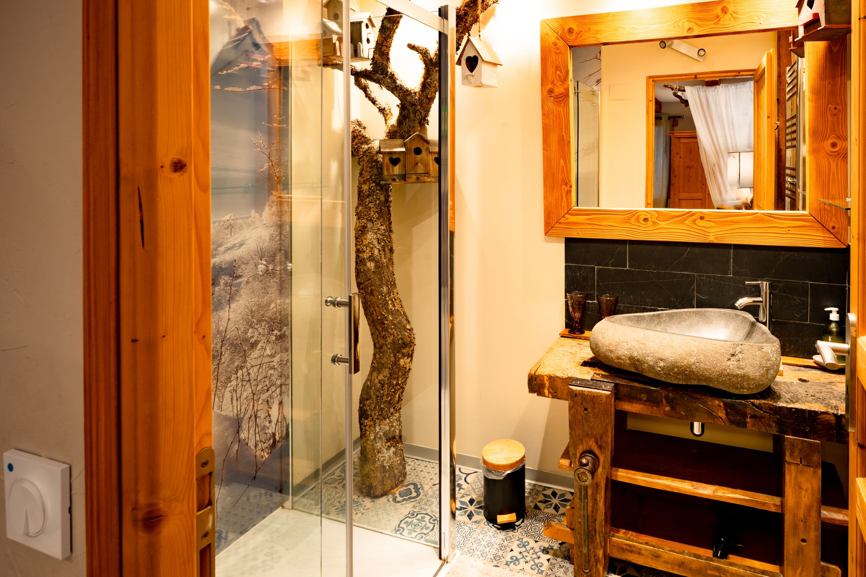A bathroom with a glass shower enclosure, a wooden vanity, and a stone sink.